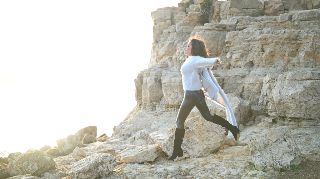 Barbie Kalev walking across coastal rocks in bright light