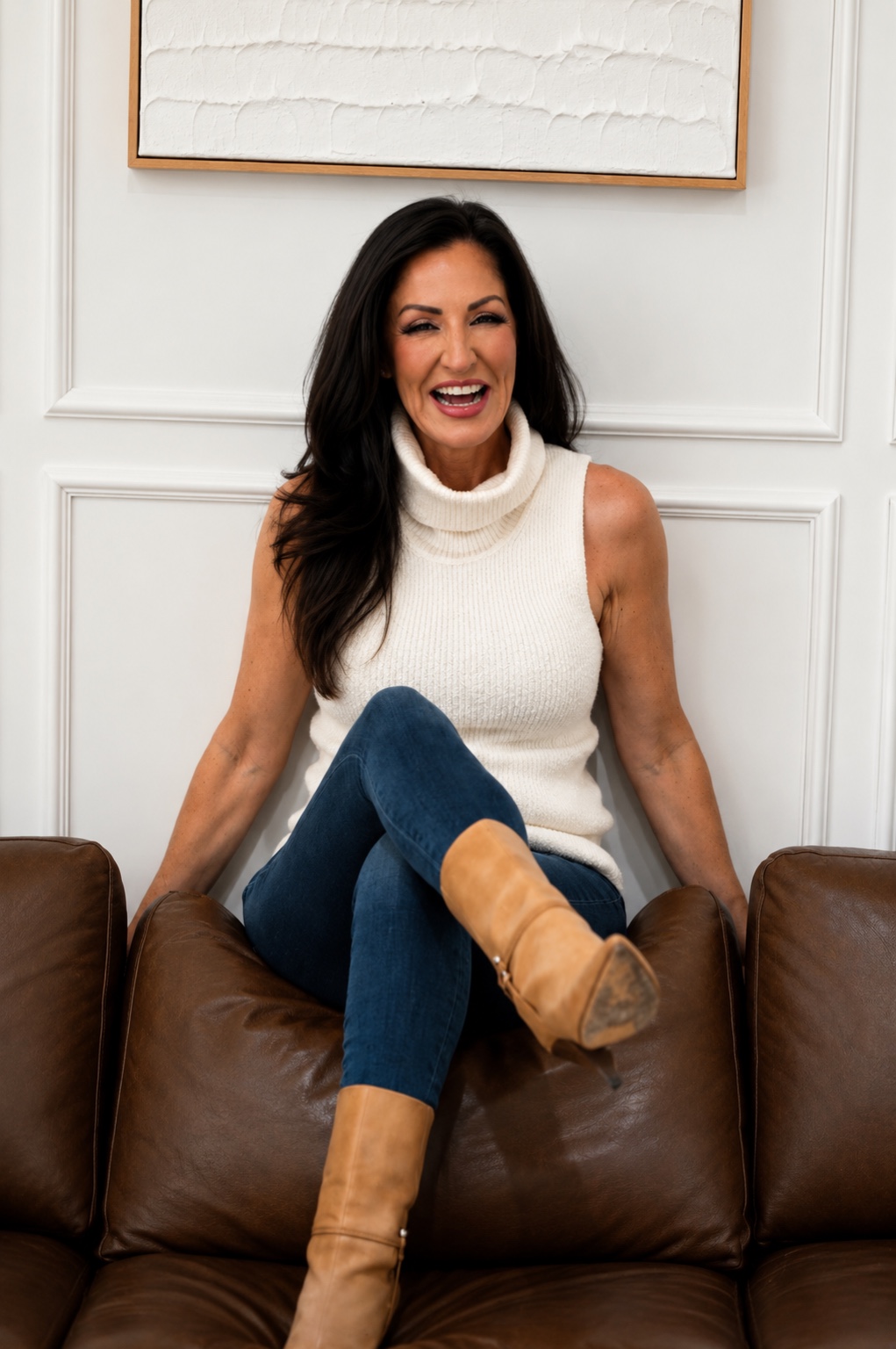 Barbie Kalev laughing while seated on a brown leather couch